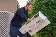 Nettoyage du boitier d'un climatiseur réversible blanc devant une maison