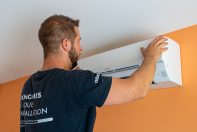 Poseur ClimeHome en train de finaliser la pose d'un climatiseur réversible blanc sur le mur orange d'une pièce