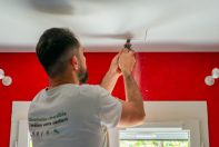 Technicien ClimeHome qui perce la plafond pour poser une grille. Les murs du pièce sont rouges et une fenêtre est devant le technicien