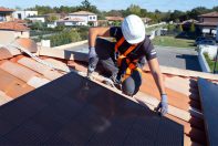 Un technicien en combinaisons de sécurité qui pose des panneaux solaires sur le toit d'une maison. Temps ensoleillé